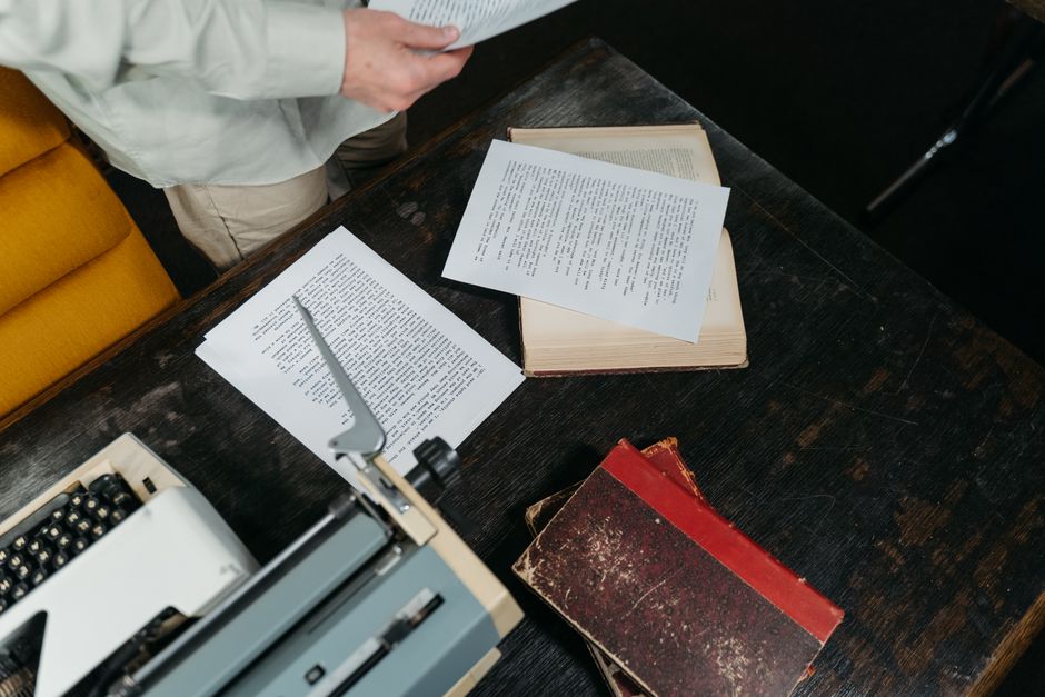 Overhead view of a classic wooden desk with a typewriter, scattered papers, and vintage books.